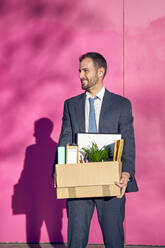 Smiling businessman with box in front of wall - VEGF05456