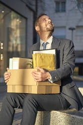 Smiling businessman with box sitting on bench - VEGF05467