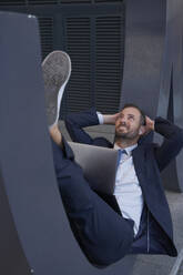 Smiling businessman lying with laptop on architectural feature - VEGF05477