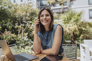 Lächelnde Geschäftsfrau, die in einem Hinterhof mit einem Smartphone spricht - MFF08746