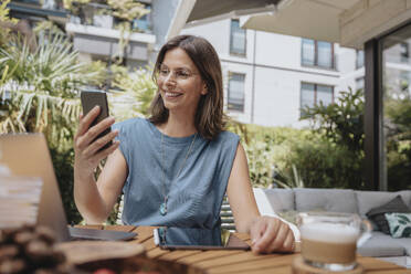 Lächelnde Geschäftsfrau bei einem Videogespräch über ihr Smartphone im Hinterhof - MFF08748