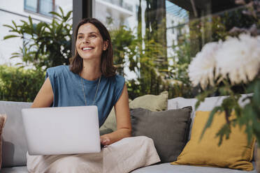 Smiling freelancer with laptop sitting on sofa - MFF08754