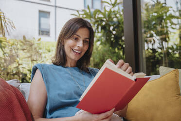 Smiling woman reading book in back yard - MFF08768