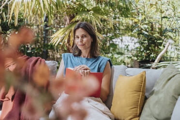 Frau mit Buch auf Sofa im Hof sitzend - MFF08770