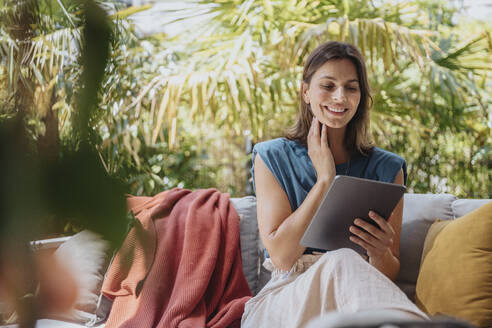 Lächelnder Freiberufler mit Tablet-PC auf dem Sofa im Hof sitzend - MFF08773