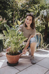 Smiling gardener kneeling by potted plant in garden - MFF08815