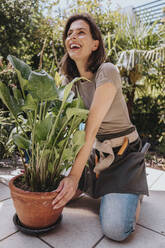 Laughing gardener kneeling by potted plant in garden - MFF08819