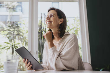Happy woman sitting with tablet PC at home - MFF08830
