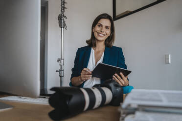 Lächelnder Fotograf mit Tablet-PC im Studio sitzend - MFF08856