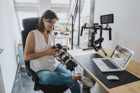 Lächelnder Fotograf, der auf einem Stuhl im Studio sitzend die Kamera überprüft - MFF08865