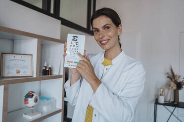 Smiling doctor pointing at eye chart in clinic - MFF08871