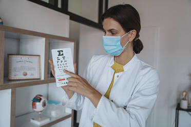 Arzt mit Gesichtsschutzmaske zeigt Augendiagramm in Klinik - MFF08872