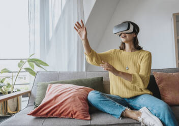 Woman with virtual reality headset sitting on sofa at home - MFF08894