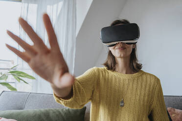 Woman gesturing wearing virtual reality headset at home - MFF08895