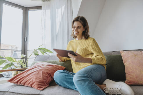 Lächelnde Frau mit Tablet-PC auf dem Sofa zu Hause - MFF08897