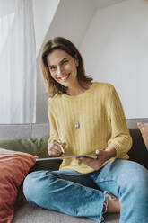 Lächelnde Frau mit Tablet-PC auf dem Sofa zu Hause - MFF08899