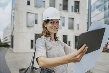 Lächelnder Architekt mit Bauplan und Tablet-PC auf der Baustelle - MFF08901