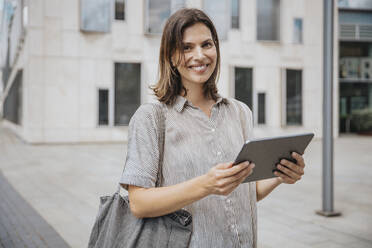 Lächelnde Frau mit Tablet-PC vor einem Gebäude stehend - MFF08906