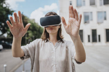 Woman gesturing wearing virtual reality headset at street - MFF08908