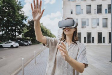 Frau gestikuliert mit Virtual-Reality-Headset vor einem Gebäude - MFF08909