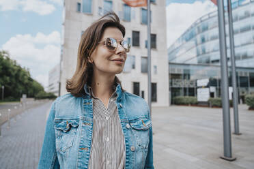 Woman in denim jacket wearing sunglasses in front of building - MFF08910