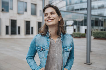 Lächelnde Frau in Jeansjacke vor einem Gebäude stehend - MFF08914