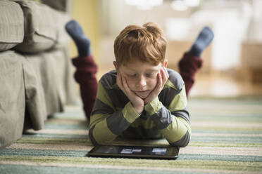 Boy (6-7) lying on carpet and using tablet pc - TETF01416