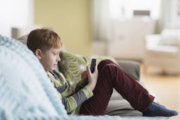 Boy (6-7) sitting on couch and using cell phone - TETF01417