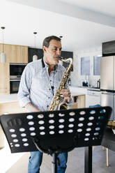 Musiker, der Saxophon bläst, vor einem Notenständer zu Hause - JRFF05332