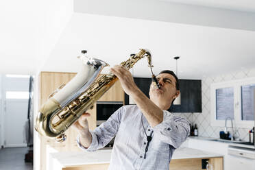 Passionate saxophonist practicing saxophone in kitchen at home - JRFF05340