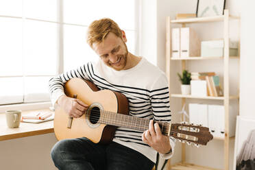 Glücklicher junger Mann spielt zu Hause Gitarre - XLGF02881