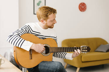 Young man practicing guitar in living room at home - XLGF02882