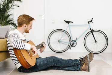 Junger Mann spielt Gitarre im Wohnzimmer zu Hause - XLGF02888