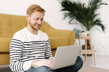 Lächelnder Mann mit Laptop auf dem Sofa im Wohnzimmer zu Hause - XLGF02893