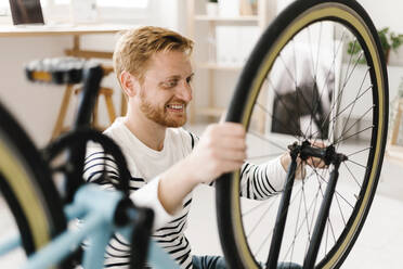 Happy young man repairing bicycle wheel at home - XLGF02898