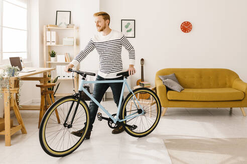Lächelnder junger Mann, der im heimischen Wohnzimmer Fahrrad fährt - XLGF02905
