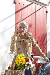 Frau mit Mantel steht mit Fahrrad an einem sonnigen Tag - VEGF05500