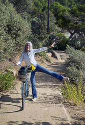 Verspielte Frau lehnt sich an ein Fahrrad und genießt den sonnigen Tag - VEGF05512