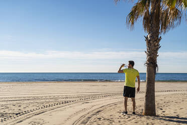 Mann trinkt Wasser an einer Palme am Strand an einem sonnigen Tag - DIGF17726