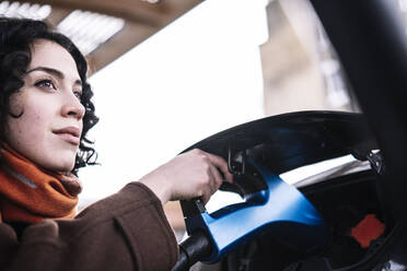 Junge Frau mit Ladegerät für Elektroautos an einer Ladestation - AMWF00201