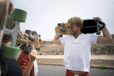 Happy friends carrying skateboards on shoulders - FBAF01845