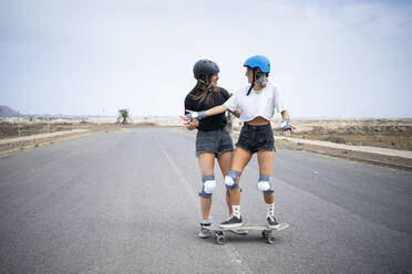 Junge Frau bringt einem Freund auf der Straße das Skateboardfahren bei - FBAF01857