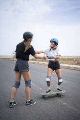 Glückliche junge Frau, die von einem Freund das Skateboardfahren lernt - FBAF01858