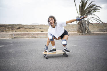 Happy young woman practicing skateboarding on road - FBAF01860