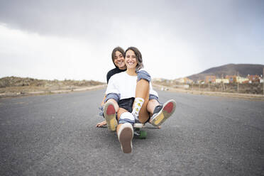 Happy friends sitting together on skateboard - FBAF01861