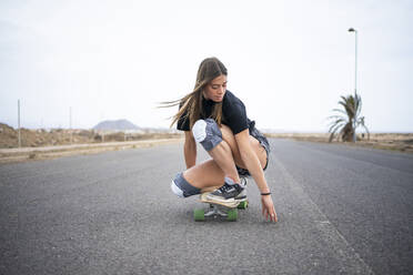 Young woman skateboarding on road - FBAF01864