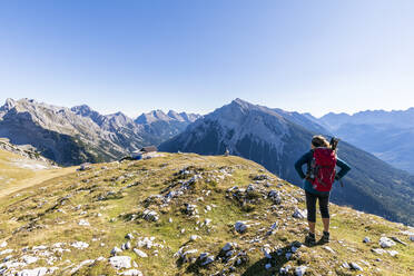 Female hiker admiring surrounding landscape from mountaintop with Tiroler Hutte retreat in background - FOF13001