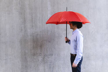 Mann mit rotem Regenschirm vor einer grauen Wand - ASGF02180