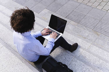 Businessman using laptop sitting on steps - ASGF02195