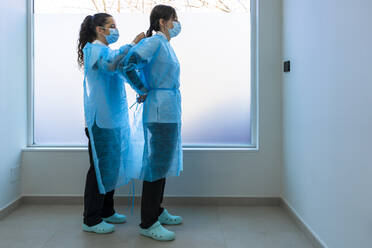 Krankenschwester hilft Arzt beim Tragen von Arbeitsschutzkleidung im Krankenhaus - DLTSF02842